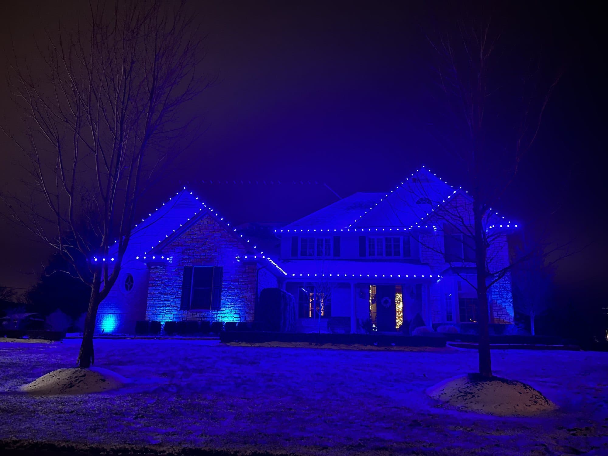 A two-story home lit with blue bulbs along every roofline
