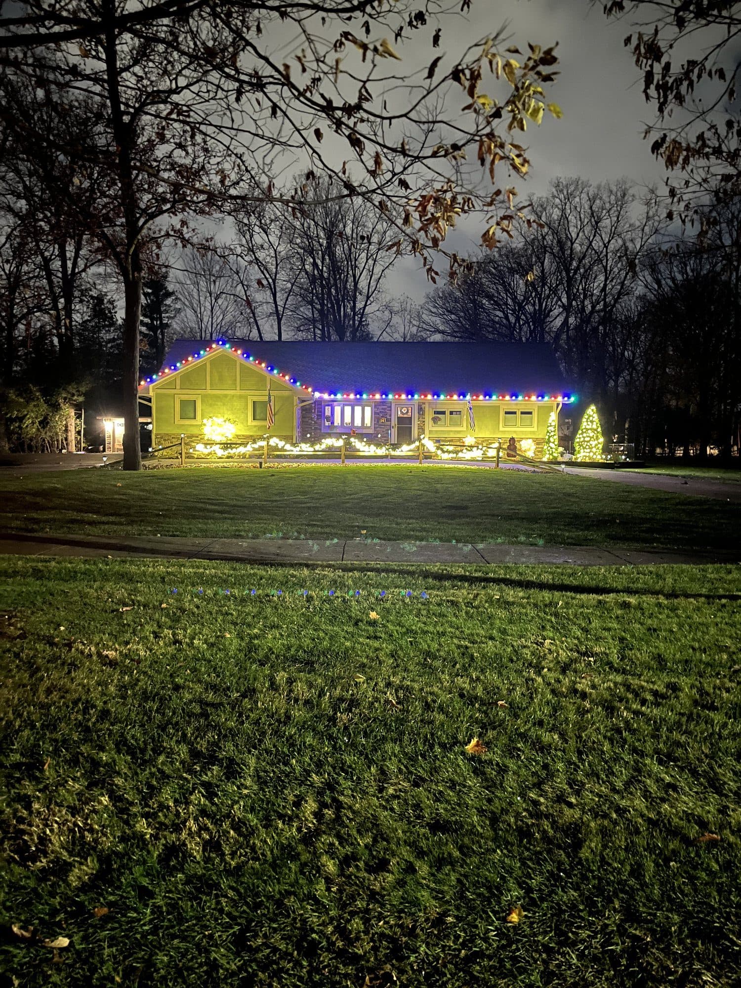 A ranch home seen across a wide lawn, warm white bulbs along the roofline