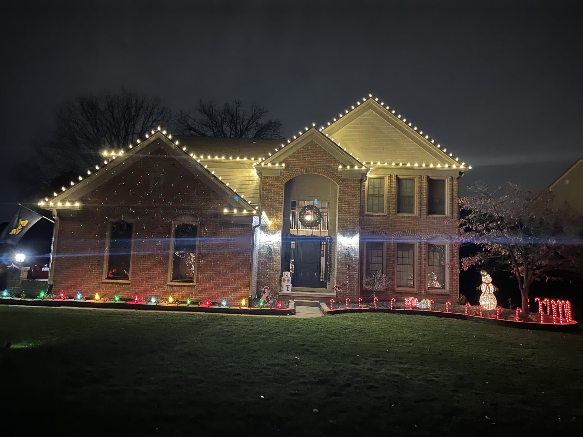 A brick colonial with warm white bulbs on every gable and multicolor lights along the front beds