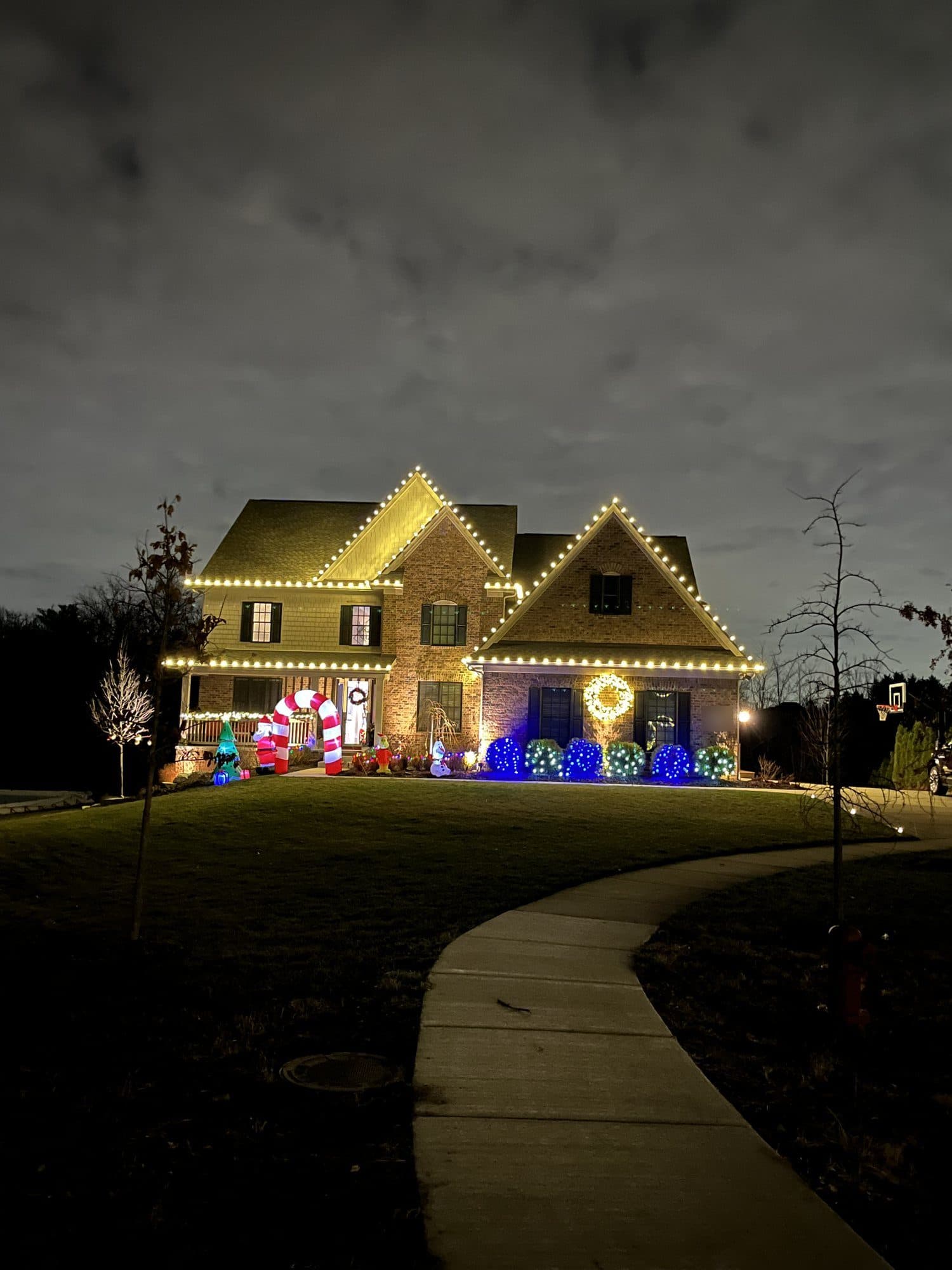 A brick and shingle home with warm white bulbs on every gable and eave, seen from the front walk