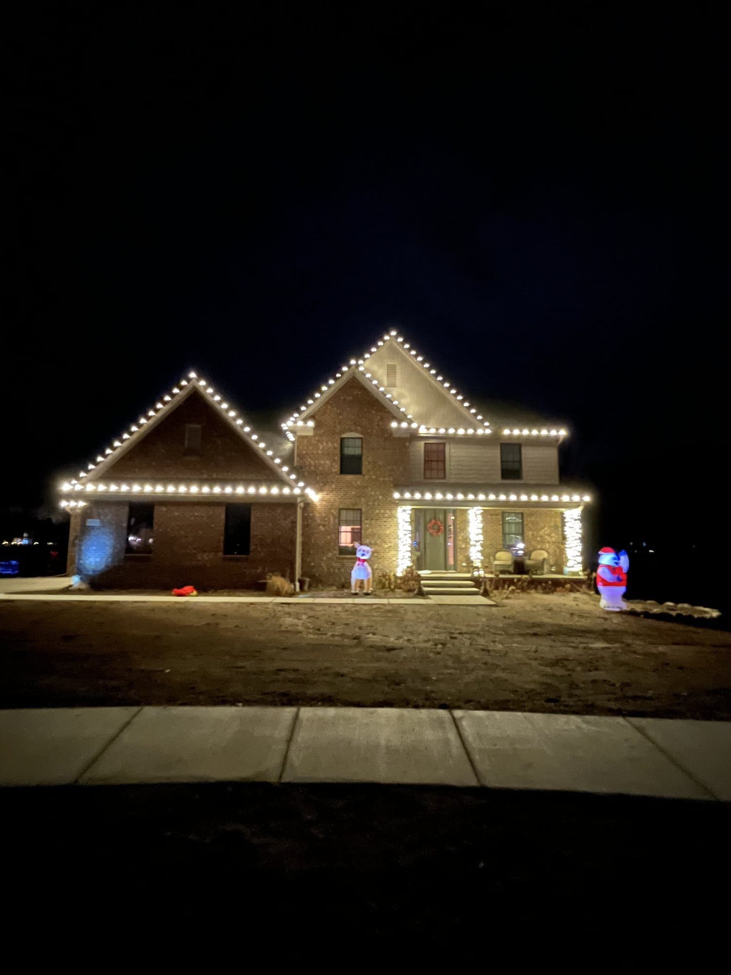 A brick home with warm white bulbs outlining two front gables and the porch
