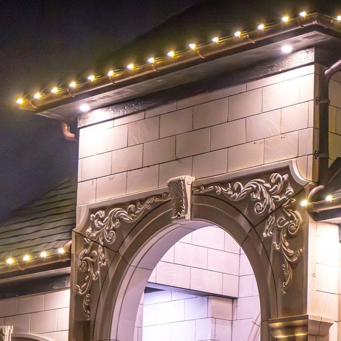 Warm white bulbs evenly spaced along a limestone eave, the run stopping where the roof edge stops