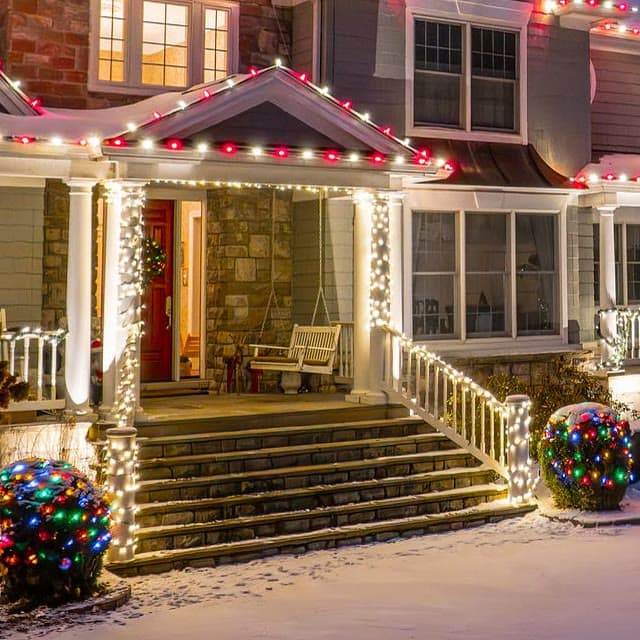 Porch columns wrapped in white lights and stair railings lined with them, under a red and white roofline