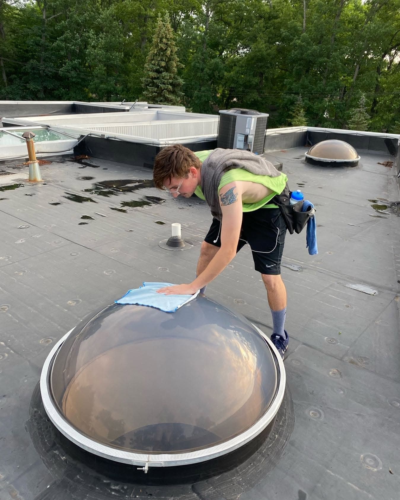 A Glass Guru technician on a flat commercial roof wiping down a clear skylight dome