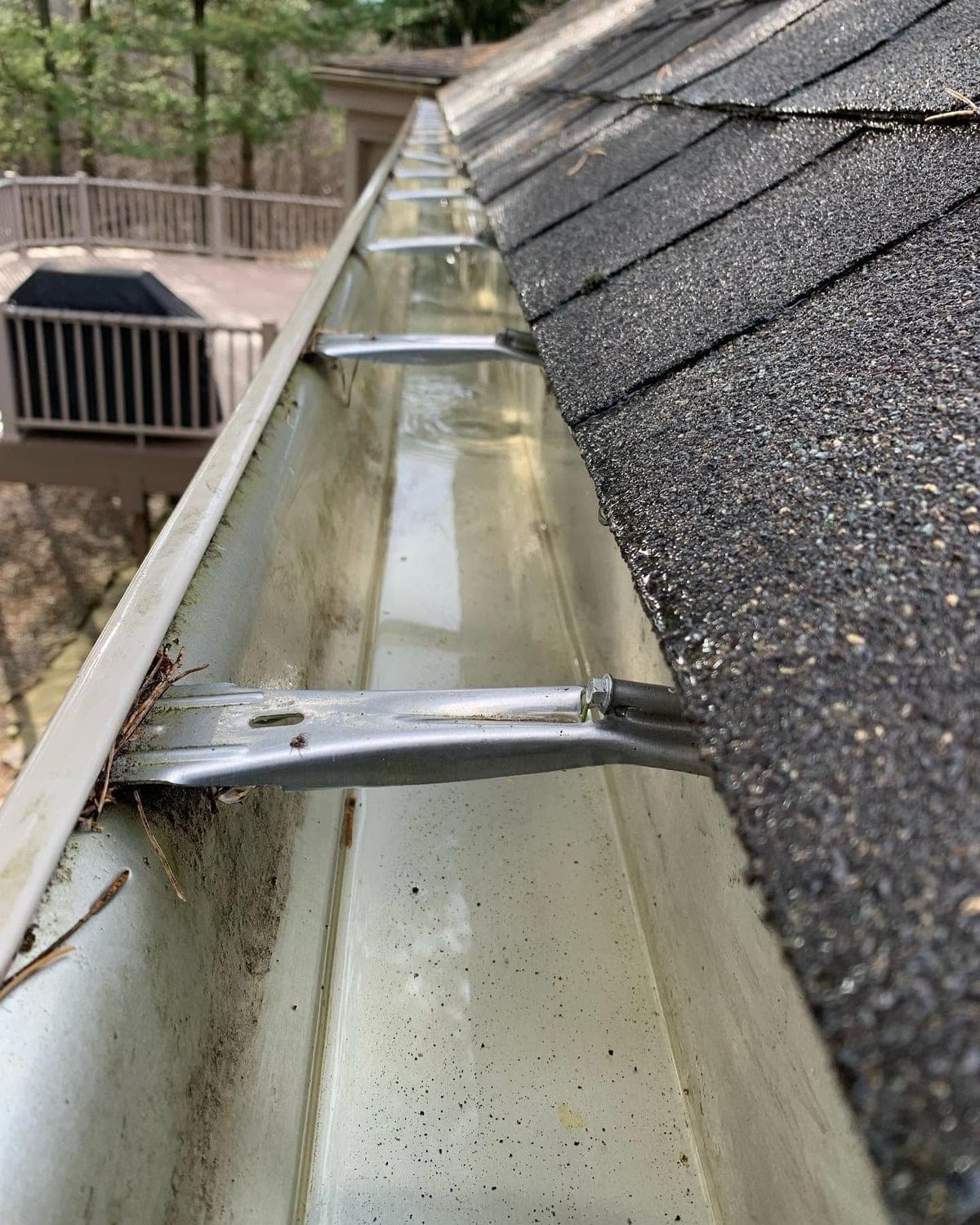 The same gutter cleared by hand, the trough empty and the downspout running free