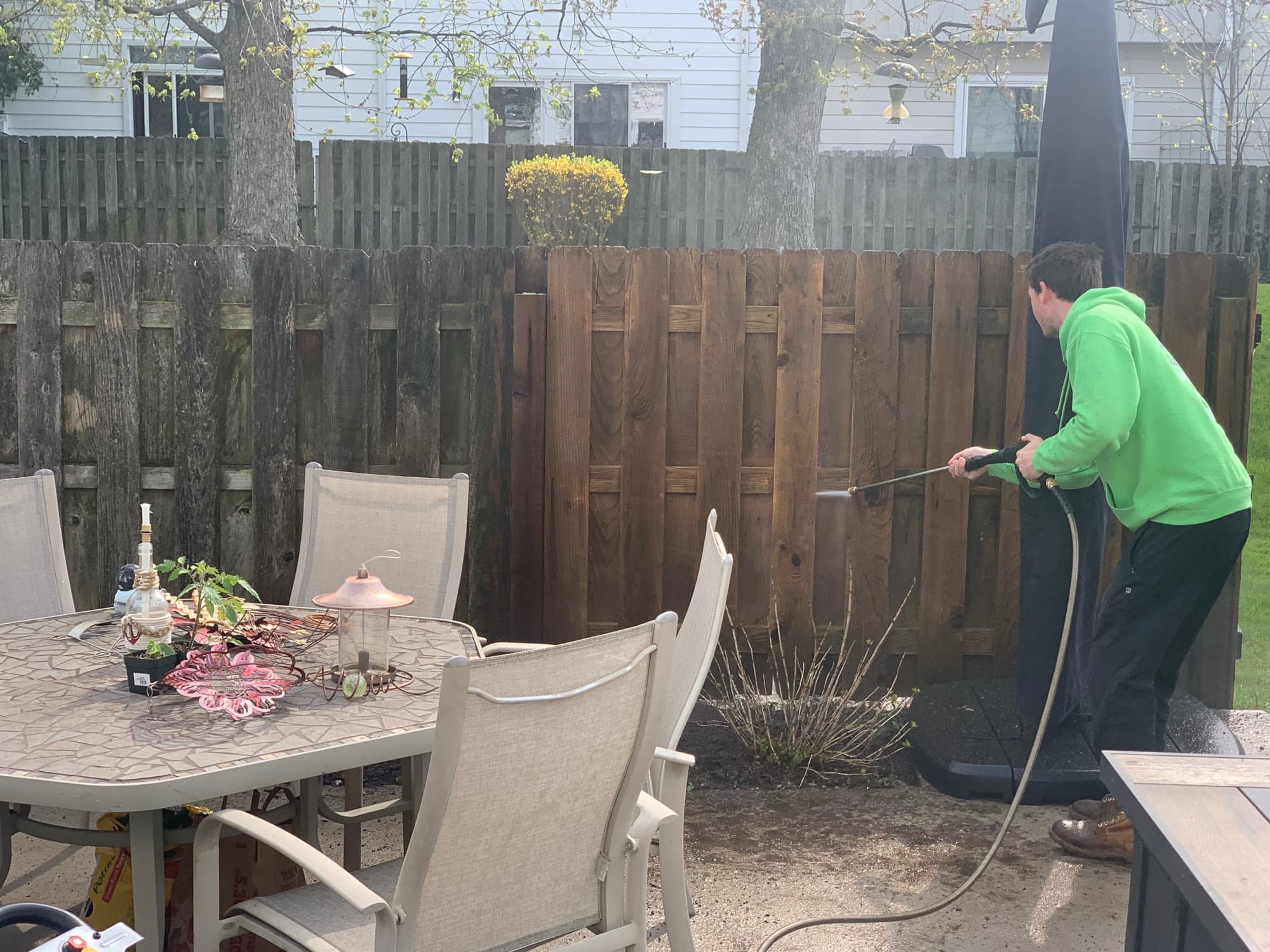 A Glass Guru technician washing a wooden privacy fence behind a patio table