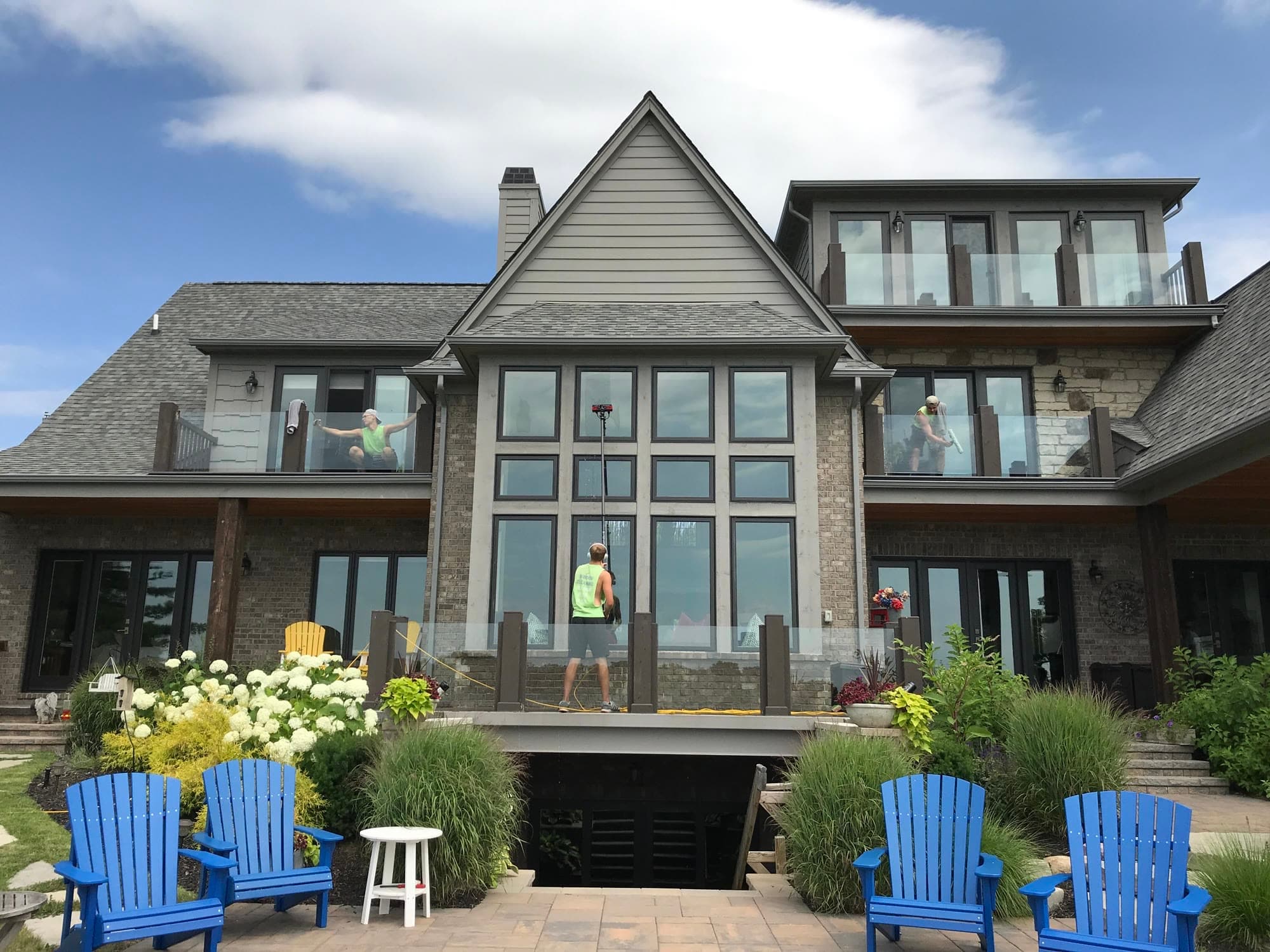 Three Glass Guru technicians cleaning the back of a house, two on the upper balconies and one on the terrace with a pole