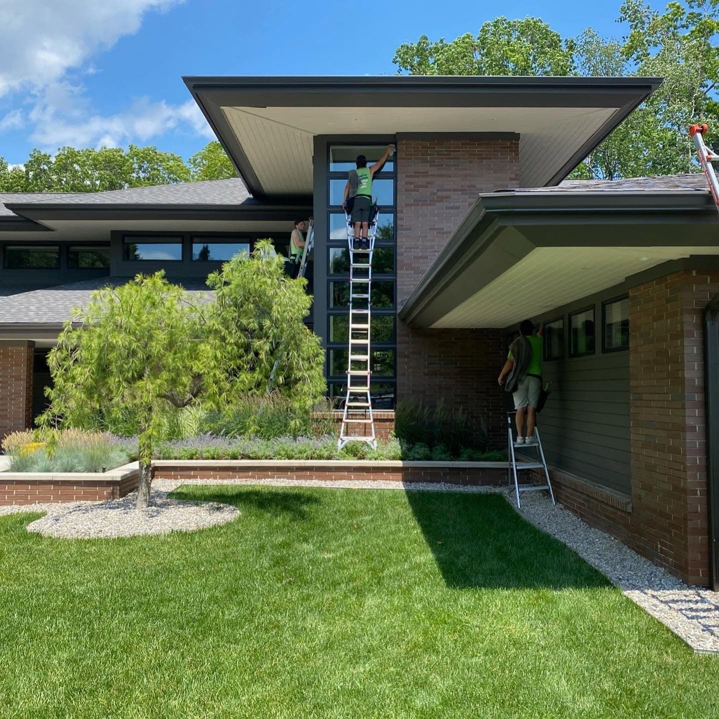 Three Glass Guru technicians on ladders cleaning the windows of a modern brick house