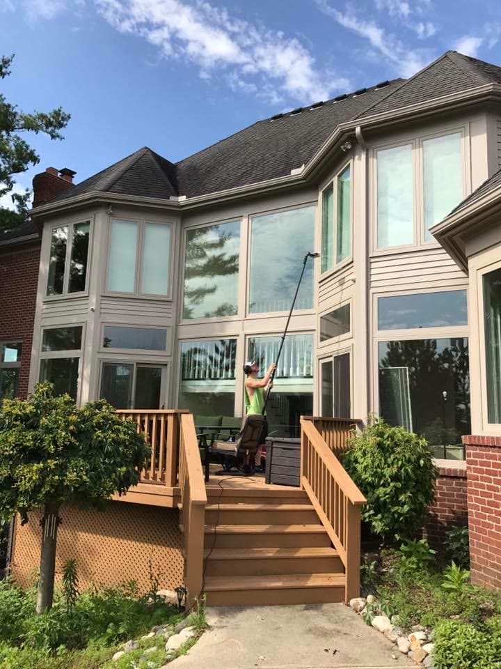 A Glass Guru technician on a back deck reaching the second-story windows with an extension pole